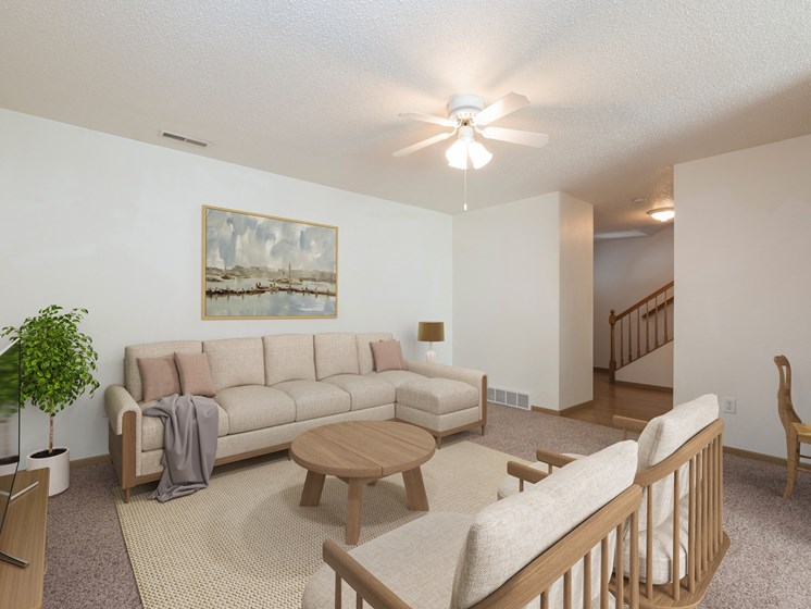 Bismarck Pebble Creek Apartments. The spacious living room is tastefully decorated with stylish furniture, ample natural light, and a cozy atmosphere. There's overhead lighting with a touch of natural light from the dining room. Access to the upstairs is in the background
